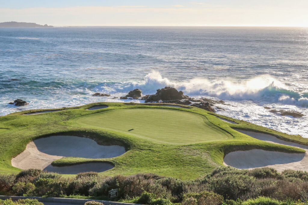 Pebble Beach Golf Links green perched above the Pacific Ocean with waves crashing along the coastline.
