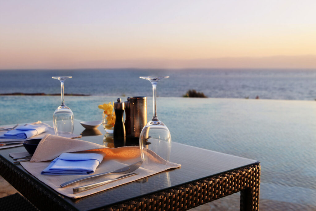 Oceanfront dining table set at sunset with wine glasses and seaside view