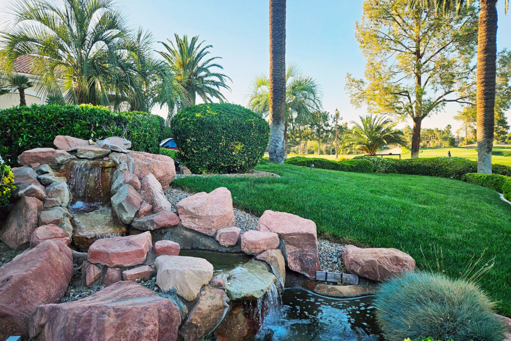 Landscaped waterfall and garden area beside a golf course with palm trees and greenery