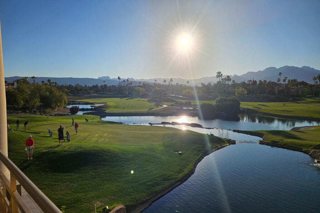 Wide view of Canyon Gate golf course with water features, golfers, and desert mountains in the distance