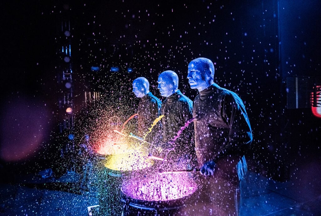Blue Man performers creating colorful paint percussion during a live Blue Man Group performance in Las Vegas.