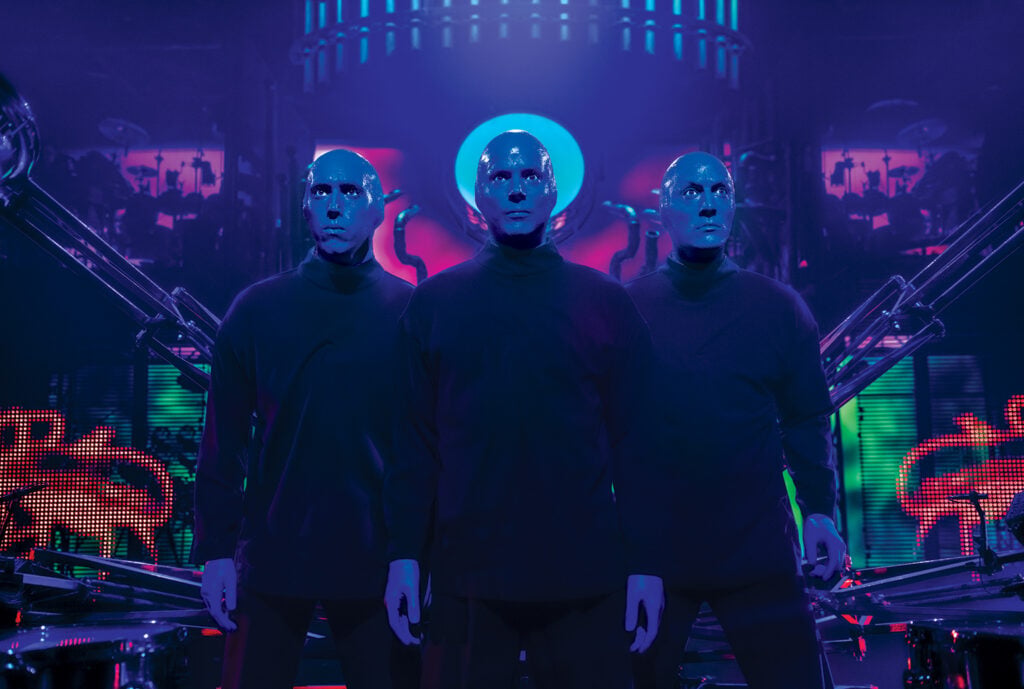 The Blue Man performers pose under dramatic lighting during a Blue Man Group performance in Las Vegas.