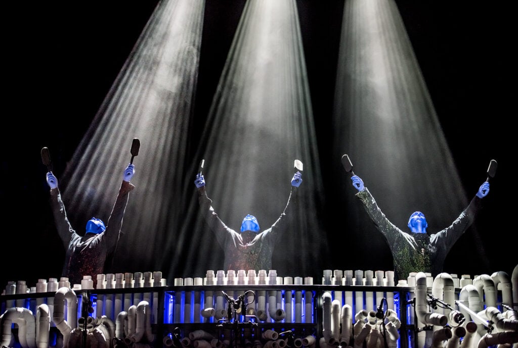 Blue Man performers under dramatic spotlights during a live musical performance at Blue Man Group in Las Vegas.