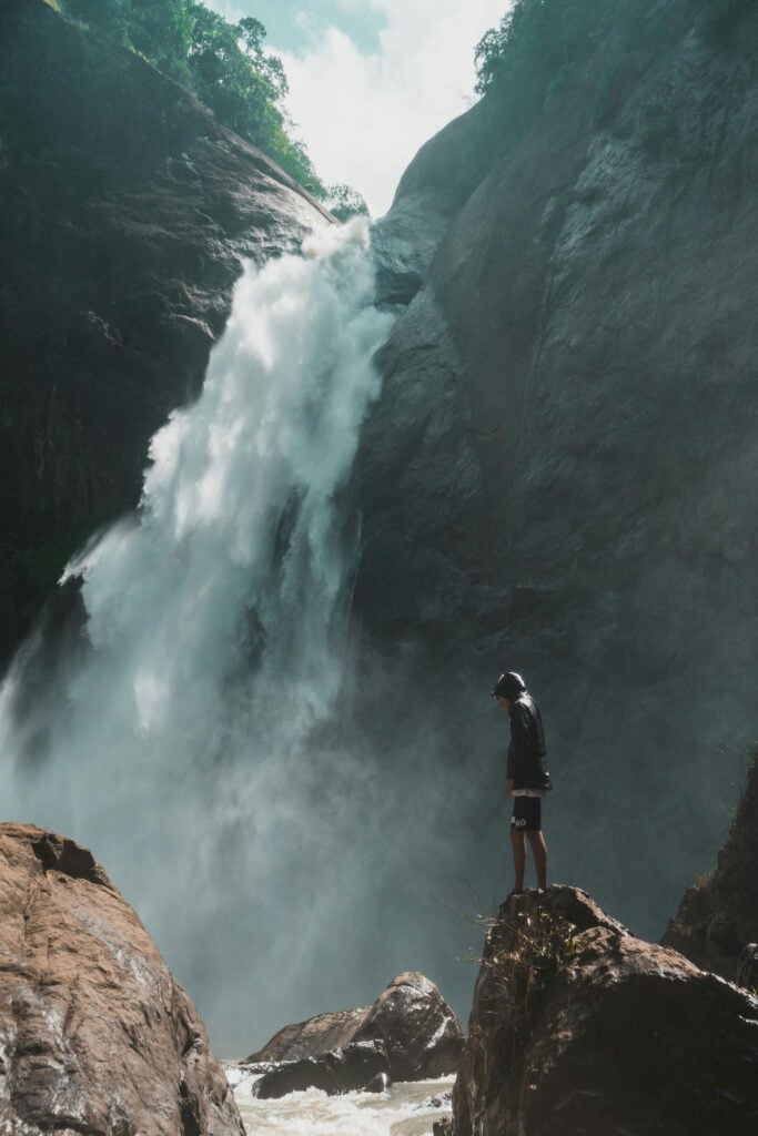 Traveler standing near a towering waterfall in a dramatic natural landscape