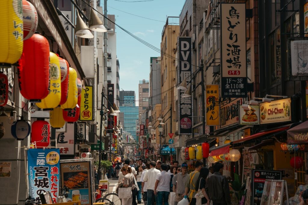 Busy shopping street lined with colorful storefronts, signs, and pedestrians in central Tokyo.