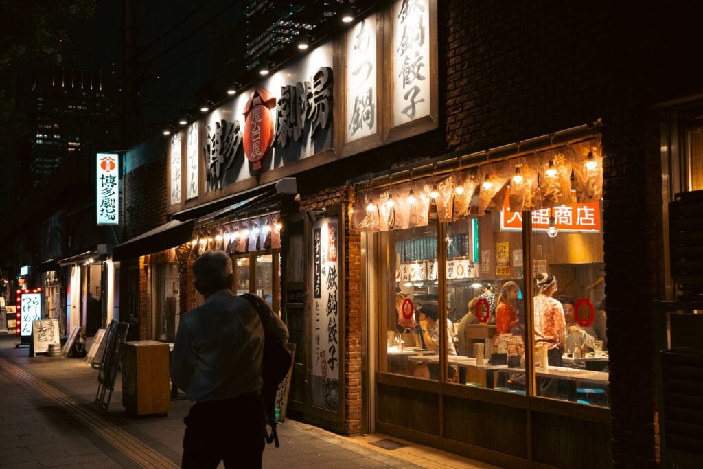 Traditional Japanese restaurant illuminated by warm lanterns along a lively street in Tokyo at night.