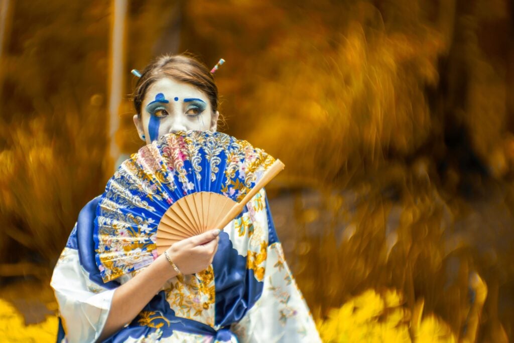 Woman dressed in a colorful traditional Japanese kimono holding a decorative folding fan outdoors.