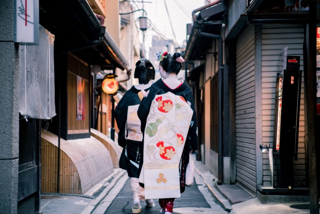 Visitors wearing colorful kimono walking along a narrow historic street lined with traditional buildings.